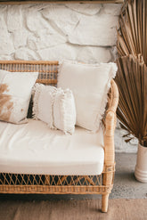 Boho rattan sofa with ivory cushions against a white stone wall