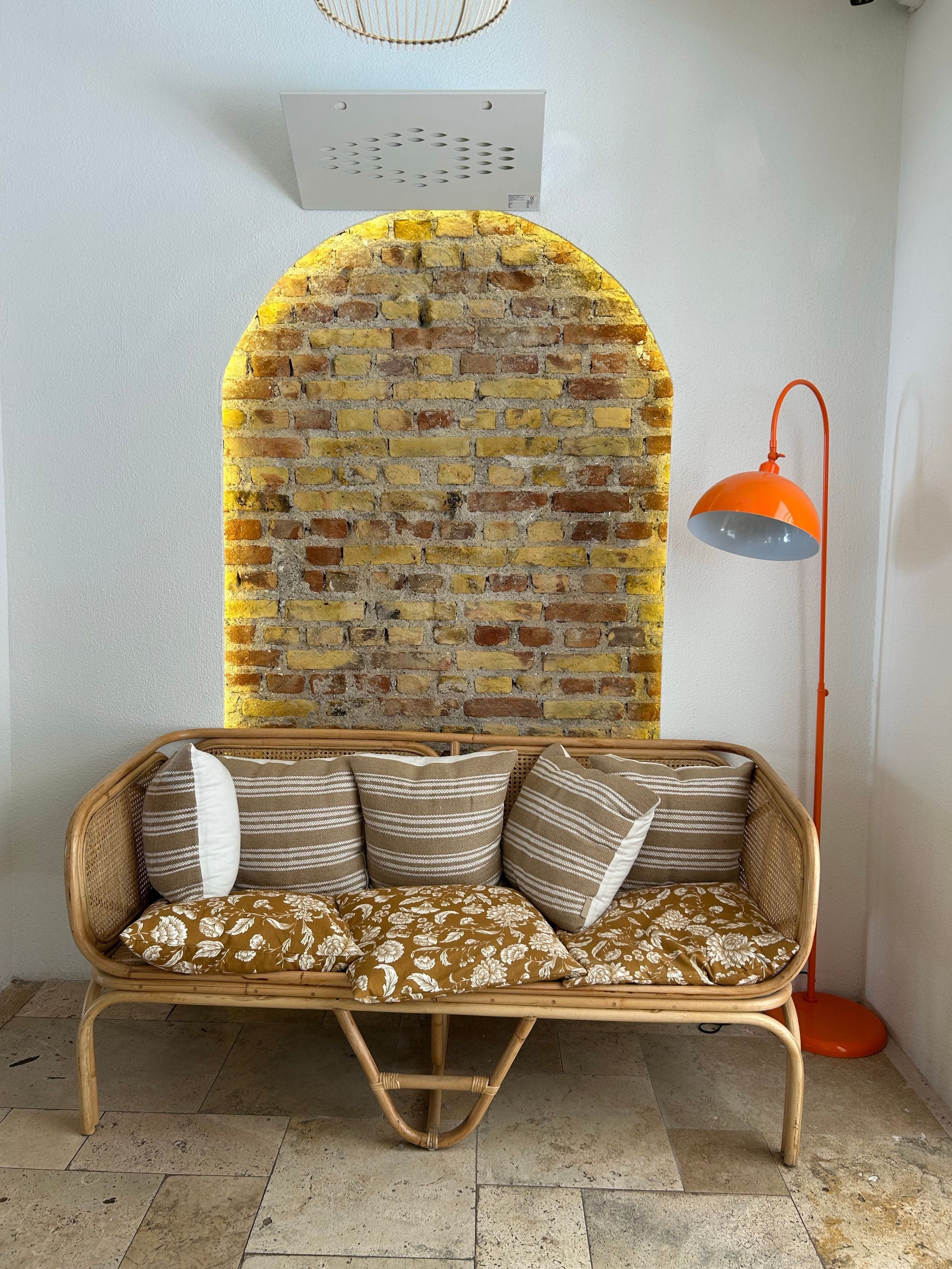 Arch rattan sofa styled under a brick archway with an orange floor lamp